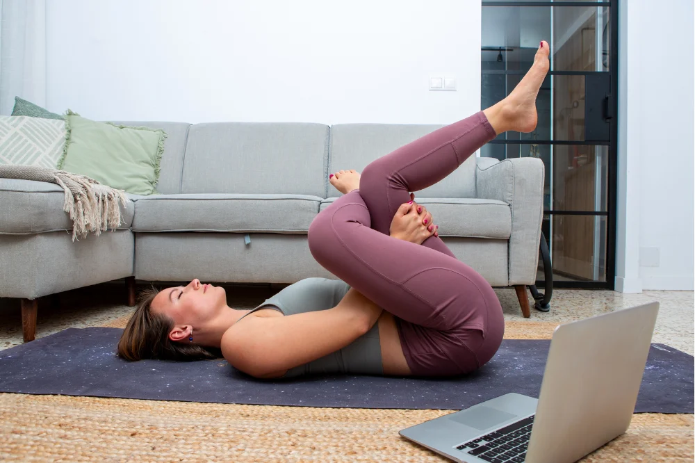 Woman lying on a yoga mat performing a supported figure-4 stretch for hip mobility