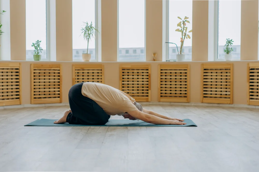 Person in child's pose on a yoga mat with arms extended, practicing restorative movement
