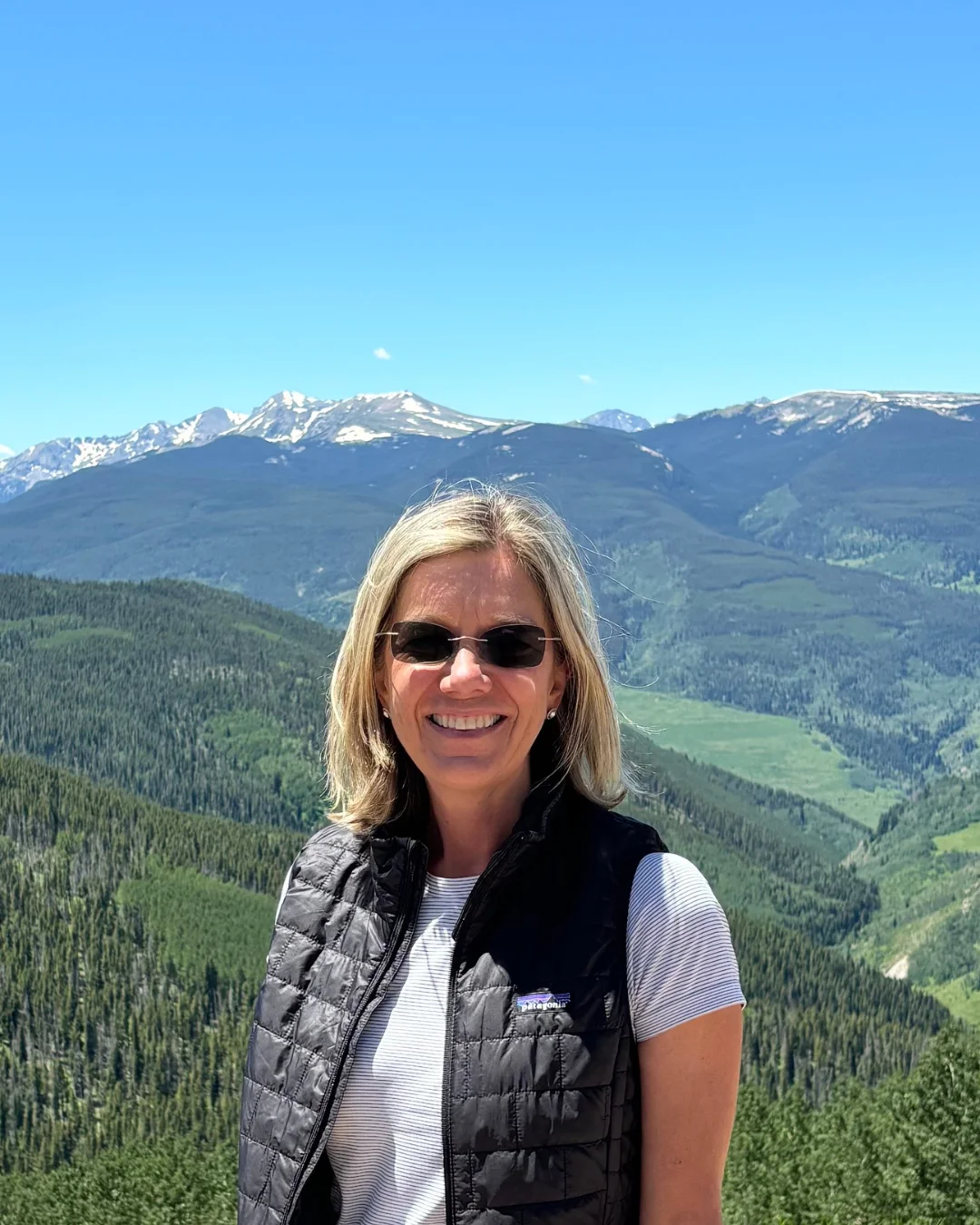 A woman smiles at the camera with a mountain range behind her