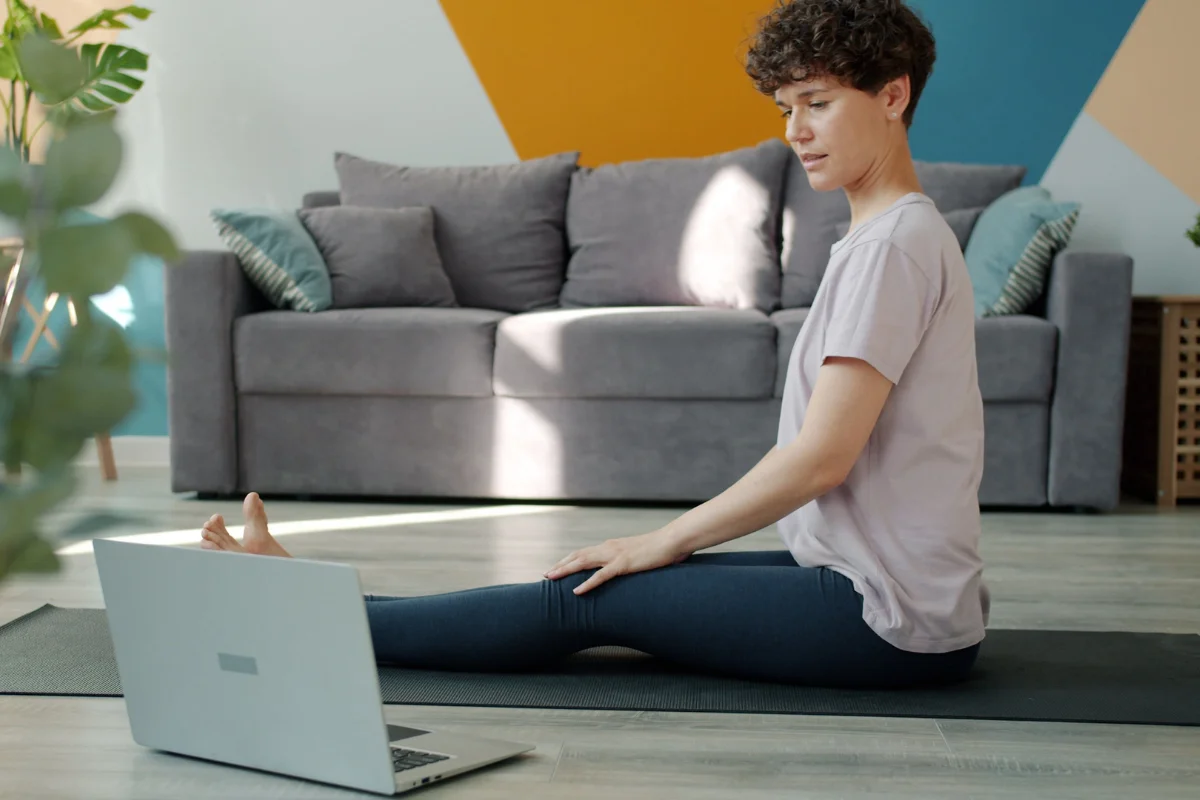 Woman doing a seated forward stretch on a mat while following an online class.