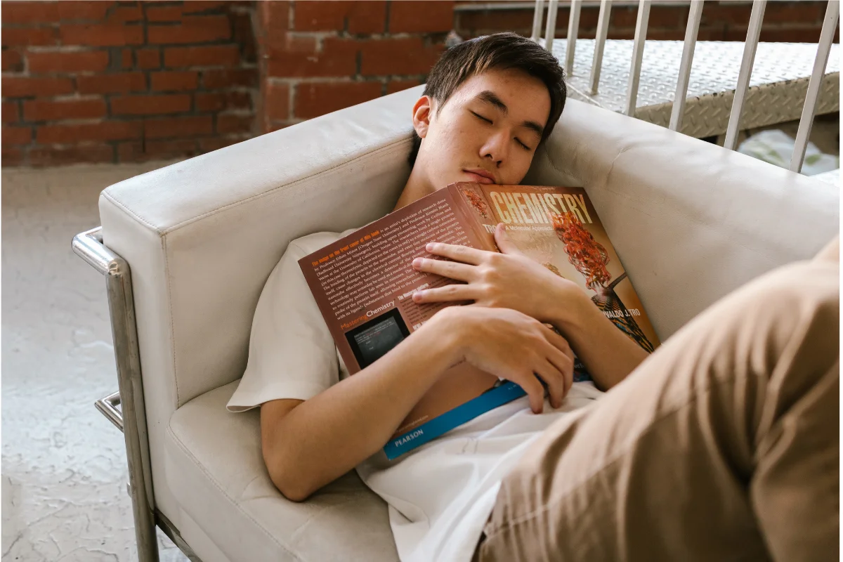 Teenager asleep on a couch, textbook in hand, showing the exhaustion that comes with hypermobility